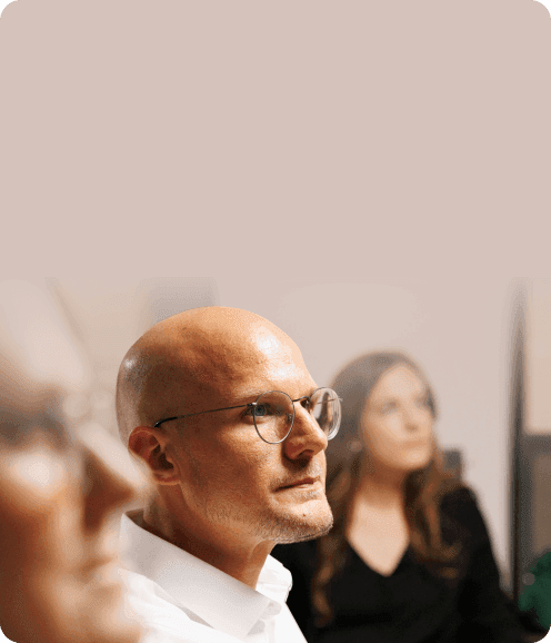 Führungskraft mit Brille im Gespräch, dahinter eine zuhörende Kollegin