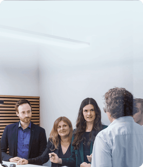 Team am Besprechungstisch: eine Kollegin erklärt, die anderen hören zu