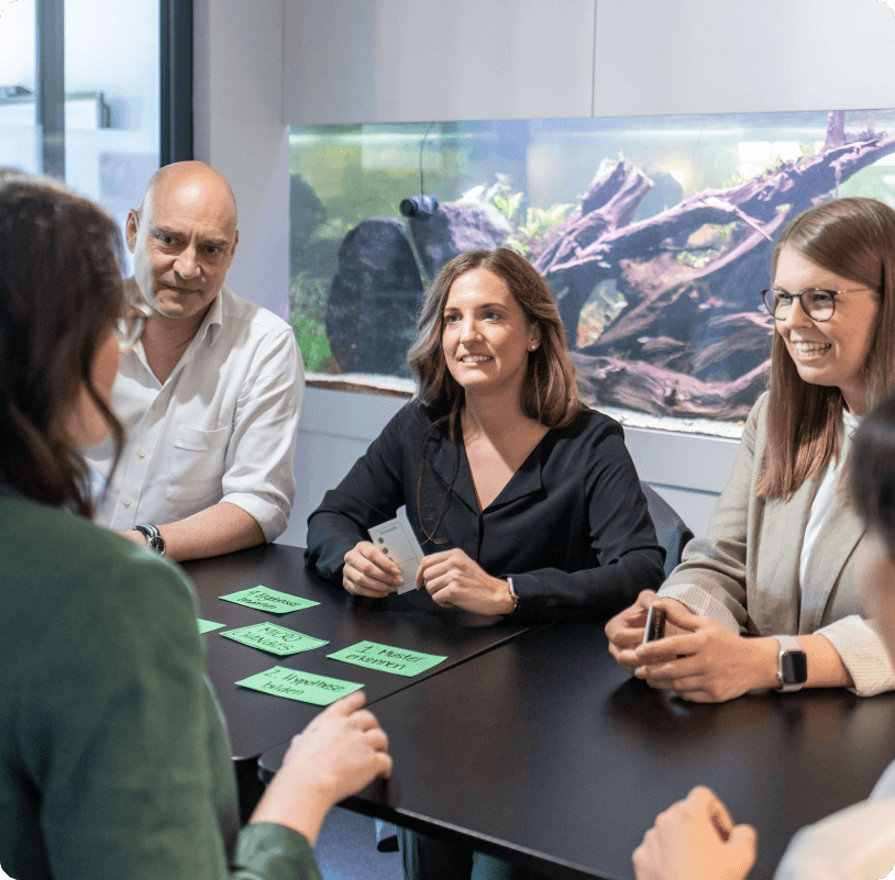 Team am Besprechungstisch sortiert grüne Karten mit einzelnen Arbeitsschritten