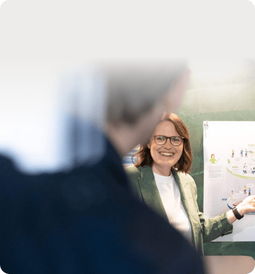 Lächelnde Frau im grünen Blazer vor einem illustrierten Poster zur Unternehmenskultur