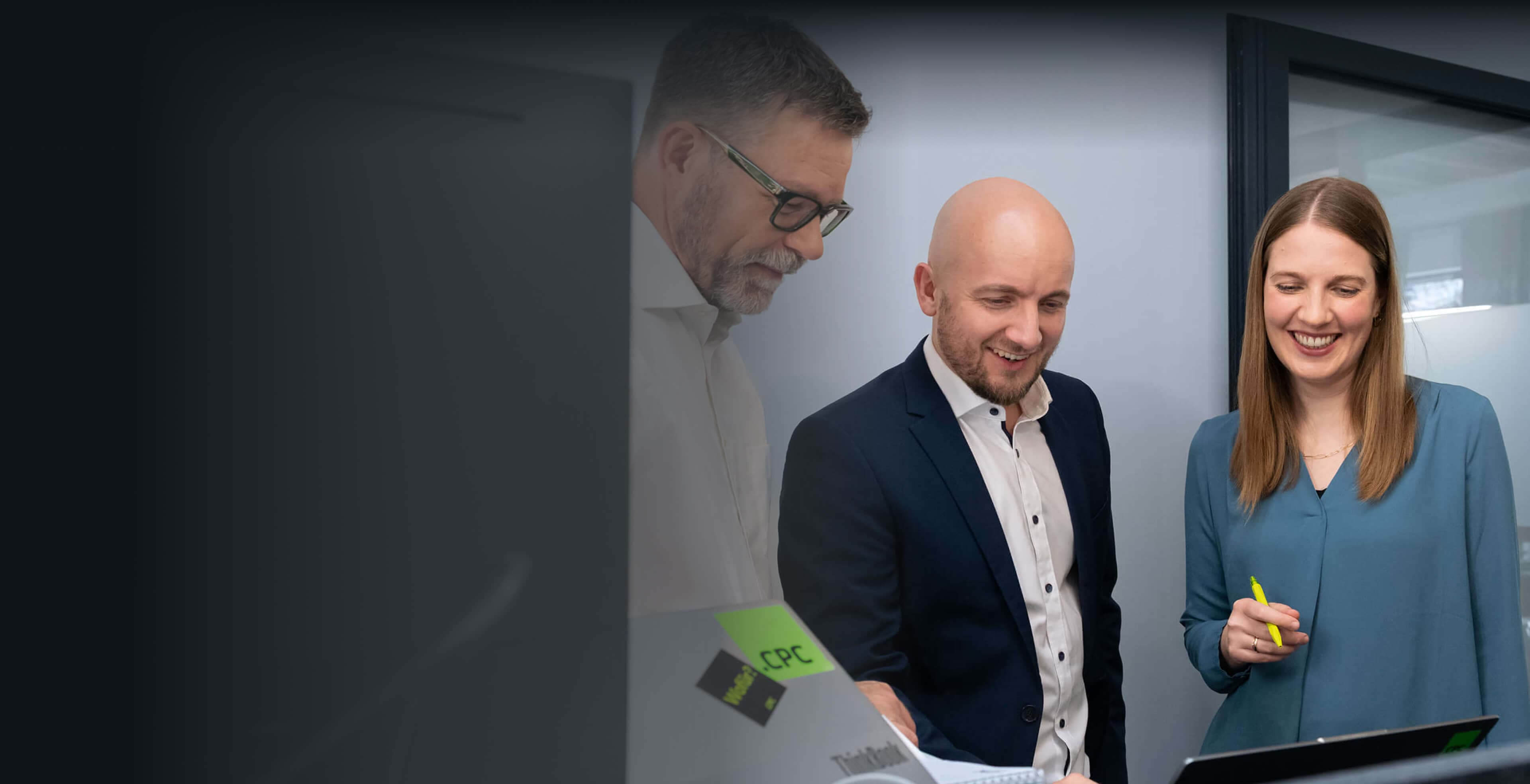 Beraterin mit Textmarker und zwei Kollegen besprechen lächelnd die KI-Strategie am Laptop