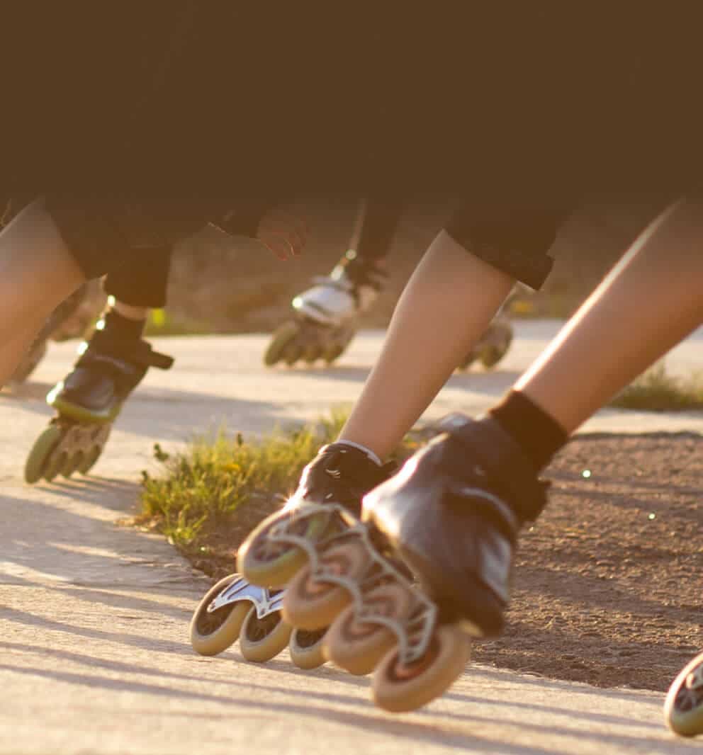 Gruppe von Inlineskatern in tiefer Hocke in voller Fahrt auf einem sonnigen Weg