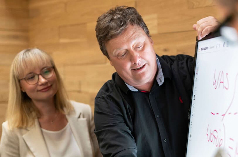 Berater erläutert einer Kollegin den Change-Prozess an einem digitalen Whiteboard