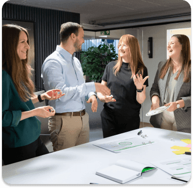 Kolleginnen und Kollegen lachen im Gespräch an einem Workshoptisch mit Arbeitsmaterialien
