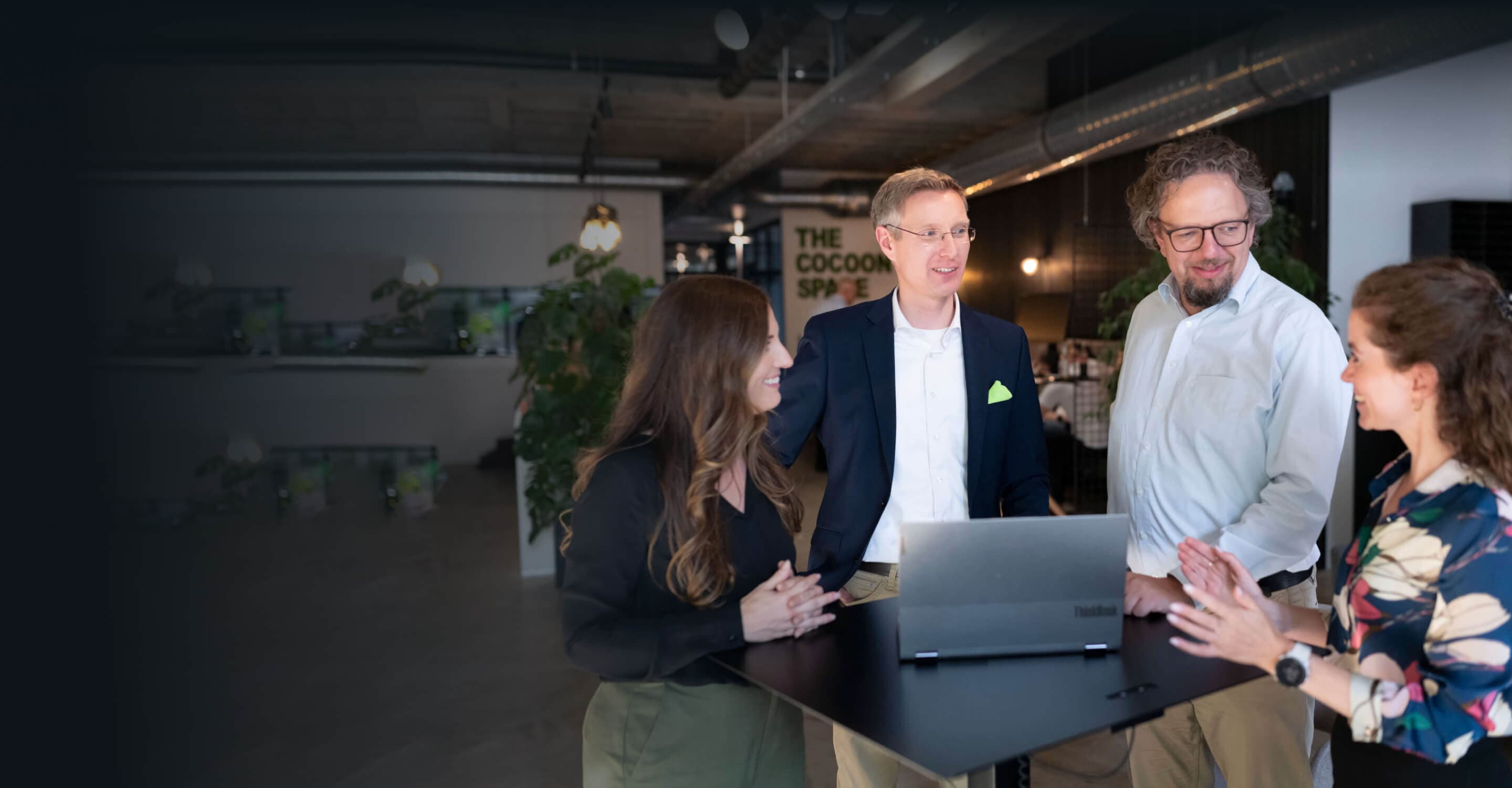 Vier Beratende an einem Stehtisch mit Laptop besprechen Change Management Modelle im Team