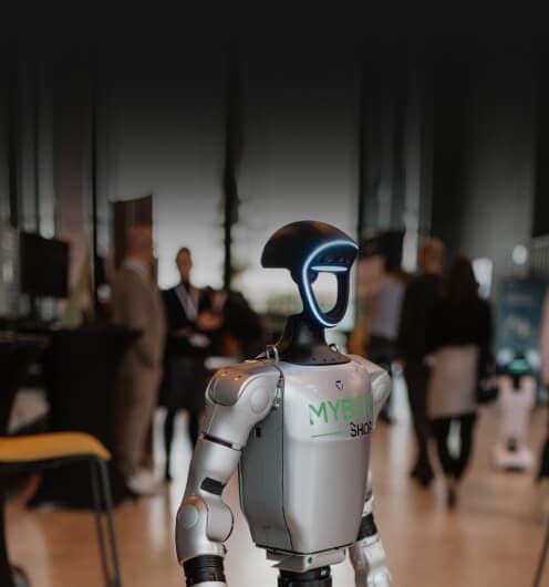 Humanoider Roboter auf einer Messe, im Hintergrund Besucherinnen und Besucher