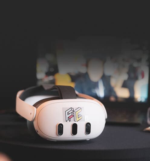 Weiße VR-Brille auf einem Tisch, dahinter ein Bildschirm