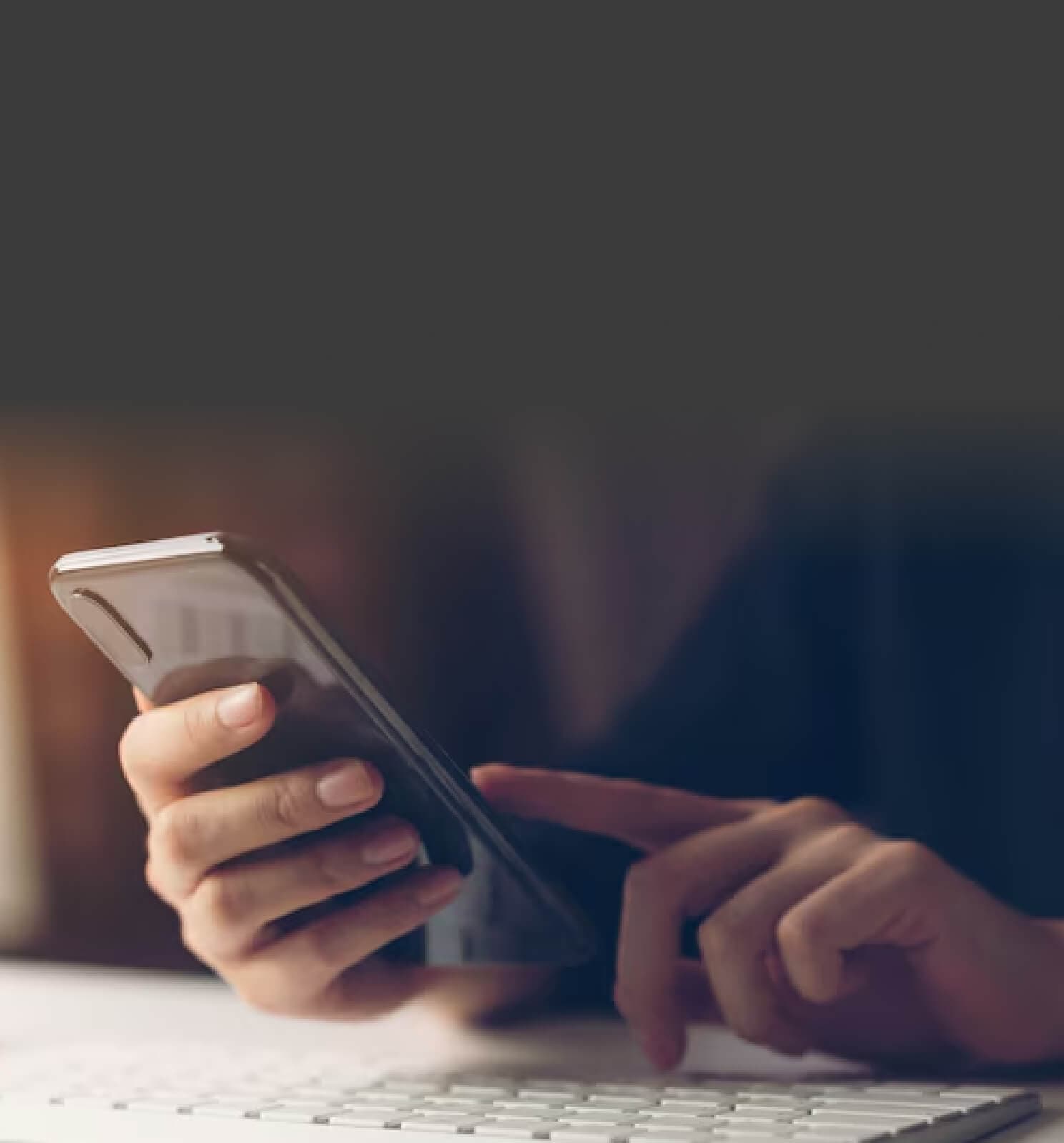 Hände mit Smartphone vor einer Tastatur