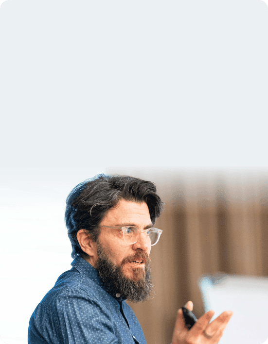 Coach mit Brille und Vollbart spricht gestikulierend zu einer Gruppe