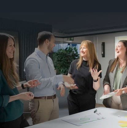 Vier Kolleginnen und Kollegen erzählen lachend am Workshoptisch mit Würfeln und Storytelling-Material