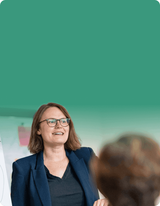 Trainerin im dunkelblauen Blazer spricht lächelnd vor einem Flipchart