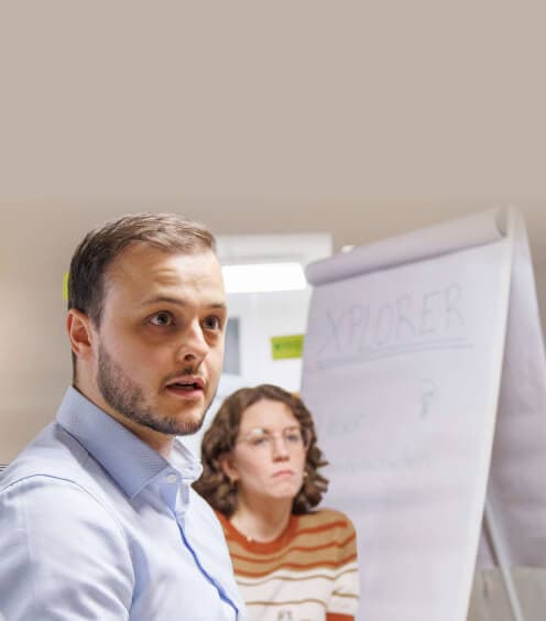 Teilnehmer spricht im Workshop, hinter ihm eine Kollegin und ein Flipchart