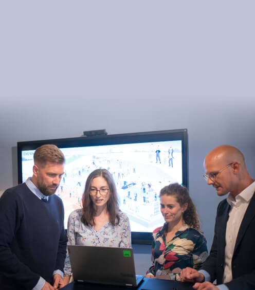Team arbeitet am Laptop vor einem großen Bildschirm mit einer Illustration